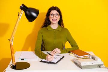 Smiling young woman working at a desk with retro objects against a vibrant yellow background