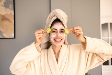 Smiling Woman in Beige Robe with Towel Head Wrap and Face Mask Enjoying Relaxing Skincare Routine