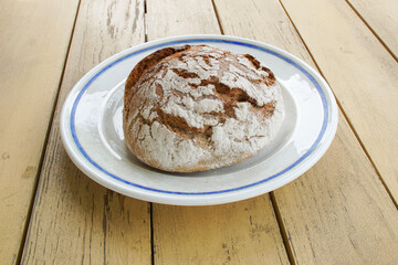 A round rye bread sprinkled with flour lies on the table on a large plate with a blue border.