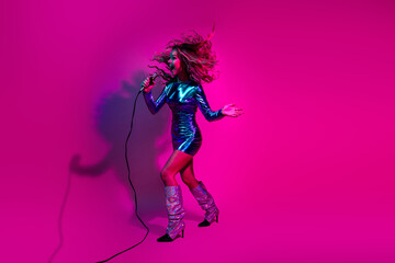 Energetic girl singing passionately in a shiny blue dress against a vivid pink background,...