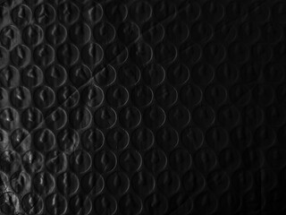 Dark, textured surface covered with evenly spaced, circular shapes creating a pattern. The lighting highlights subtle contours and shadows, adding depth and an abstract feel