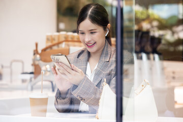 Asian Young woman smiling happily using smartphone in cafe