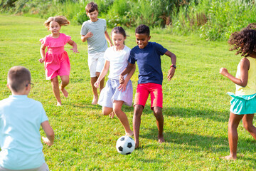 Obraz premium Positive kids running on field and playing football together.
