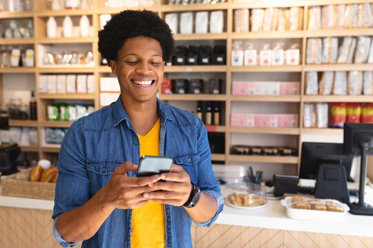 African American man standing behind wood-front counter at cafe holding smartphone among pastries