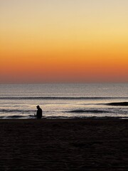 Silhouette of person standing alone at the edge of the ocean during a calm sunrise in Virginia Beach