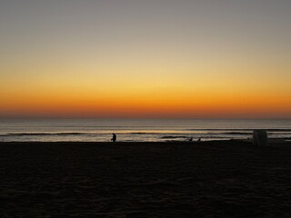 Silhouette of person standing alone at the edge of the ocean during a calm sunrise in Virginia Beach