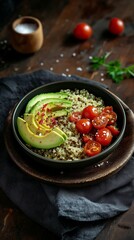 A healthy quinoa bowl topped with avocado and cherry tomatoes sits on a wooden table. Black linen and pink salt details add rustic charm and culinary contrast.