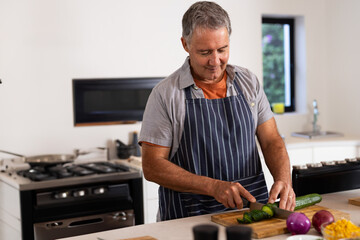 Senior man slicing cucumber into thin rounds at kitchen island with wooden cutting board