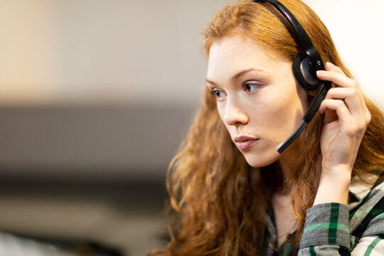 Female call center agent adjusting headset microphone while working at office desk, copy space