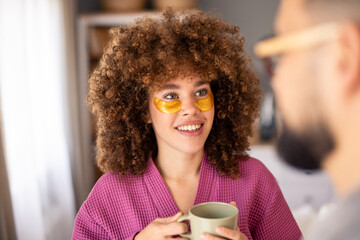 Happy Woman in Pink Bathrobe with Under-Eye Patches Enjoying Coffee Indoors