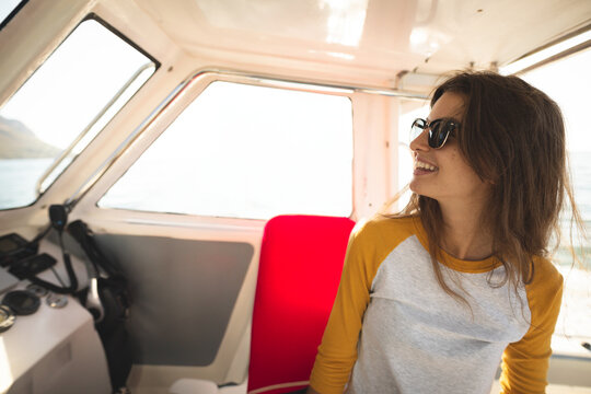 Teen female sitting on red seat in boat cabin wearing sunglasses near control panel, copy space