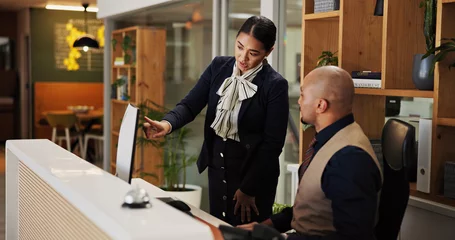  Man, woman and concierge with mentor at hotel with computer, point and discussion for booking info. People, training and receptionist with listening with pc for hospitality with coach at lodge © peopleimages.com