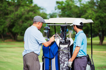 Senior golfer coaching young man golfer on fairway during sunny morning. Family bonding and sport mentoring while choosing the right golf club for outdoor practice.