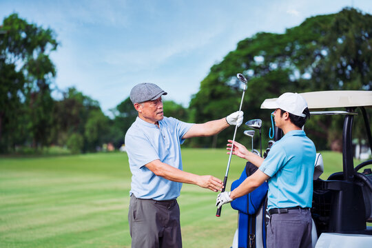 Senior golfer coaching young man golfer on fairway during sunny morning. Family bonding and sport mentoring while choosing the right golf club for outdoor practice. - Powered by Adobe