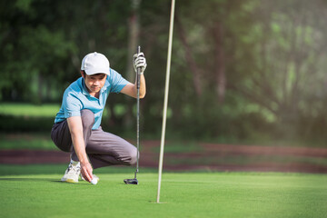 Golfer preparing to putt golf ball into the hole on green grass at golf club during summer, focusing on precision and balance.