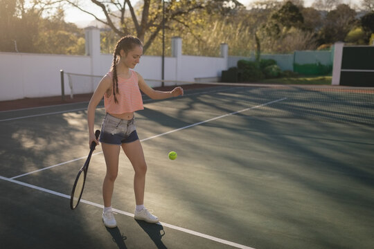 Athlete is bouncing ball on green court, holding racket near net under warm afternoon sun