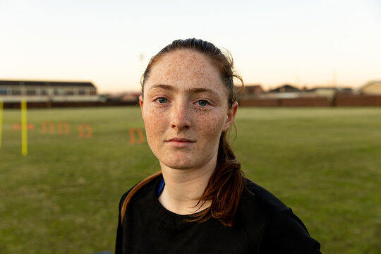 Teenage female athlete training on grassy training field at dusk with orange hurdles, yellow pole