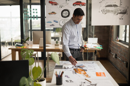 Male designer standing at table reviewing car concept sketches in design studio with drafting tools