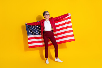 Elderly woman with stylish outfit holding an American flag and showcasing patriotism on a yellow background