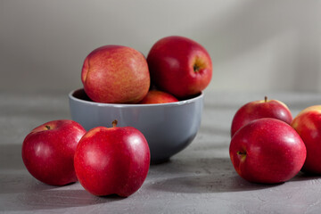 A gray ceramic bowl filled with red apples sits on a textured gray surface, with several apples scattered around it. Soft natural light create a calm, minimalist food scene. Proper nutrition concept 