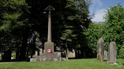 Fototapeta premium Stone cross war memorial with a red poppy wreath standing in a cemetery in Helmsley, UK, in the North York Moors National Park