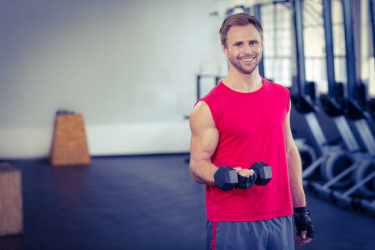 Male trainer lifting hexagonal dumbbell near plyometric boxes and rowers on mats in gym, copy space