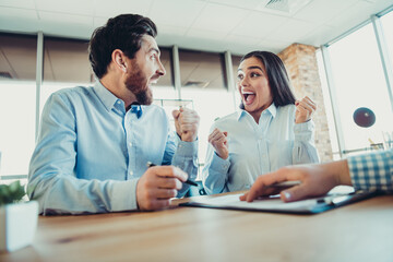 Excited coworkers celebrating success together in modern office space during collaborative teamwork meeting