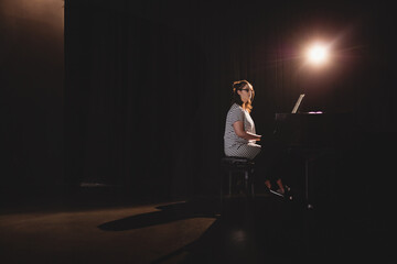 Grand piano resonating under warm spotlight on theater stage with sheet music displayed, copy space