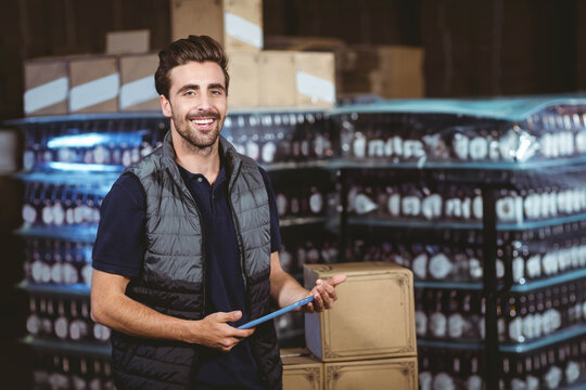 Male inventory worker smiling and holding light blue clipboard in warehouse with pallets