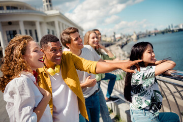 Group of cheerful young friends enjoying a sunny day by the waterfront during a summer outing in the city