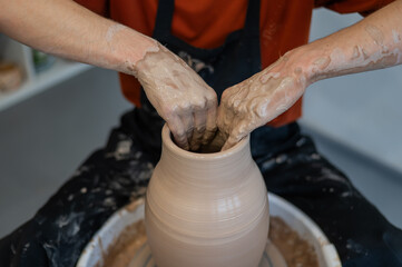Close-up of a potter's hands making a ceramic vase on a potter's wheel. 
