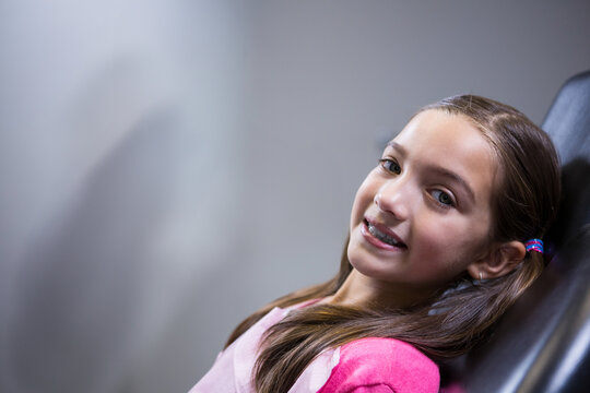 Girl reclining, smiling in dental chair at clinic with braces and colorful elastics copy space