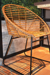A modern rattan chair with a rounded backrest and black metal legs stands on a tiled floor, casting...