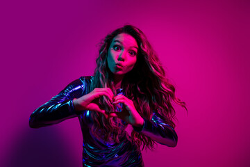 Glamorous young woman girl in a blue dress making a heart symbol against a bright neon pink background