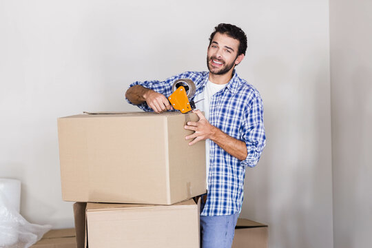 Man holding tape dispenser and sealing cardboard box in empty room with bubble wrap, copy space