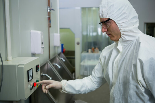 Male cleanroom technician pressing red button on control panel by sinks in lab, copy space