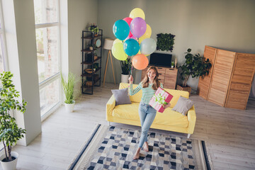 Young woman holding colorful balloons and a gift in a cozy living room with cheerful decoration
