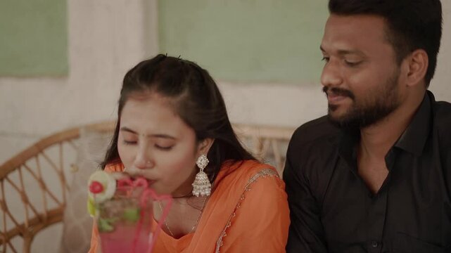 An affectionate Indian couple shares an intimate moment outdoors, dressed in traditional ethnic attire. The woman wears a bright orange salwar suit while the man is in a black shirt and jeans. 