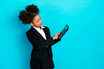 Confident schoolgirl in formal uniform using calculator against turquoise studio background, promoting education and knowledge
