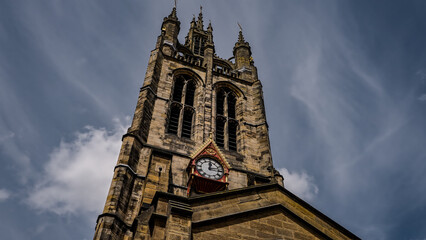 Low angle view of St. Nicholas Cathedral's majestic tower and clock against a backdrop of dynamic clouds