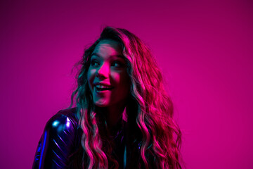 Young girl with blonde hair in a shiny blue dress, smiling against a vibrant pink background, perfect for nightlife and fashion advertising