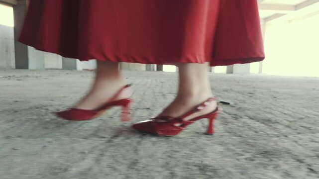 Low-angle tracking shot of a woman's red high heels walking on a gritty concrete floor. A cinematic clip about fashion, confidence, and determination.
