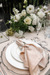 Beautiful table setting featuring white plates, a blush napkin with a glass holder, and polished silver cutlery. Glasses are neatly arranged, creating a sophisticated dining atmosphere.