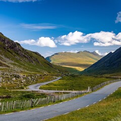 Winding Road Through Green Valley with Mountains Under Blue Sky and White Clouds - Scenic Landscape Photography