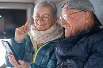 Cheerful modern senior couple sitting on a bus while looking together at smartphone sharing tech and social