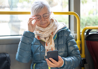 Portrait of a modern senior woman dressed in winter clothes sitting on the passenger seat  on a bus...