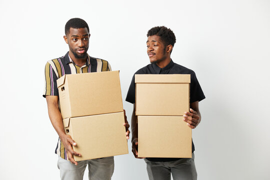 Two African American men carrying cardboard boxes, looking puzzled and surprised. Their expressions convey curiosity and confusion, lending a humorous touch to the scene.