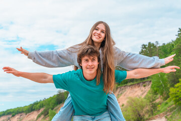 A young couple teenagers, a girl and a boy outdoor, laughing and smiling, Piggyback ride with open...