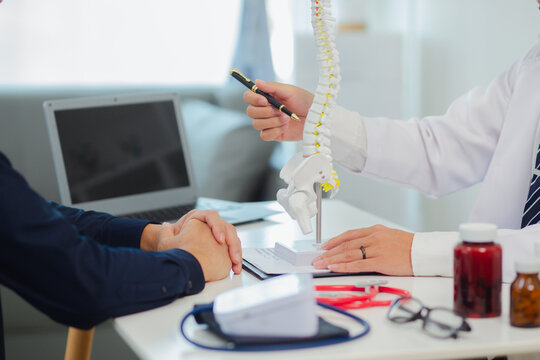 An orthopedic doctor shows a spinal model to a patient in a human spinal hospital. Diseases and disorders of the spinal cord, back pain, lumbar pain, orthopedic surgery, chiropractic, office syndrome - Powered by Adobe