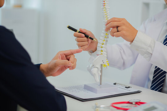 An orthopedic doctor shows a spinal model to a patient in a human spinal hospital. Diseases and disorders of the spinal cord, back pain, lumbar pain, orthopedic surgery, chiropractic, office syndrome